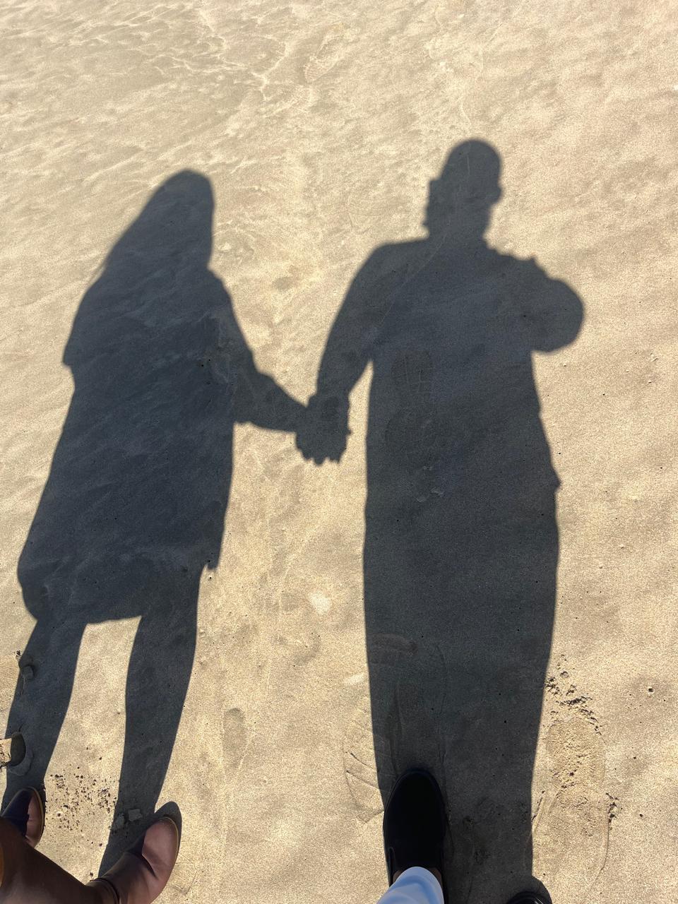 Two shadows holding hands on sand as a symbol of relationship and support